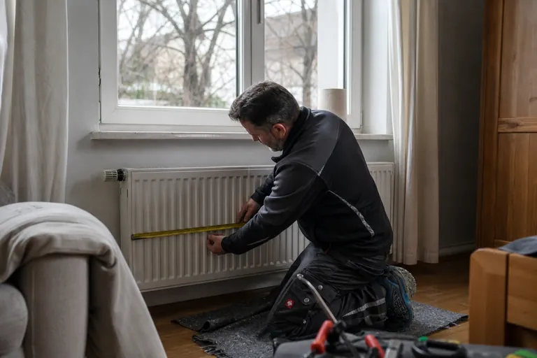 Monteur misst die Höhe und Länge eines Plattenheizkörpers in einem Altbauzimmer