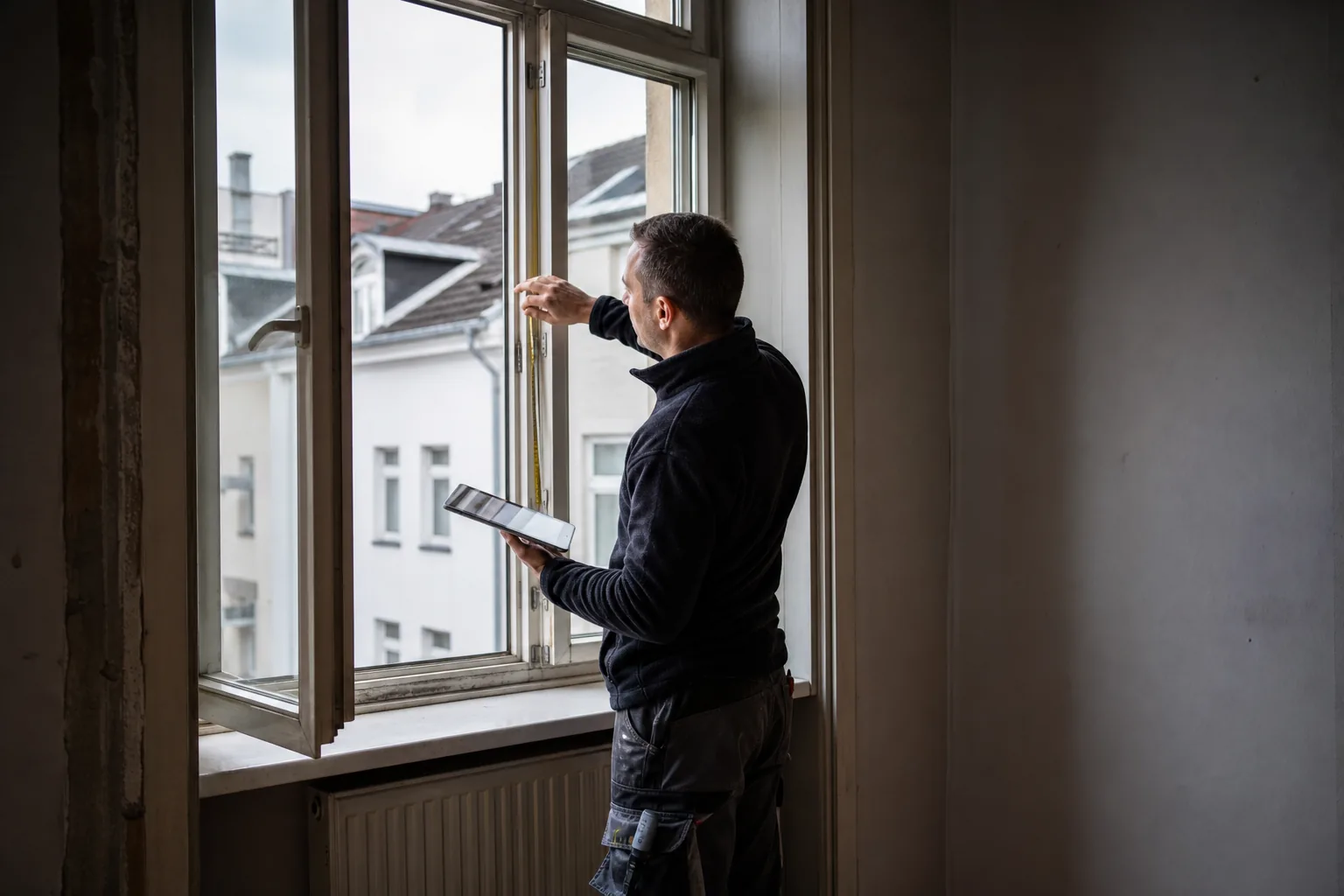 SHK Fachkraft erfasst Maße eines Fensters in einem Altbauzimmer auf einem Tablet